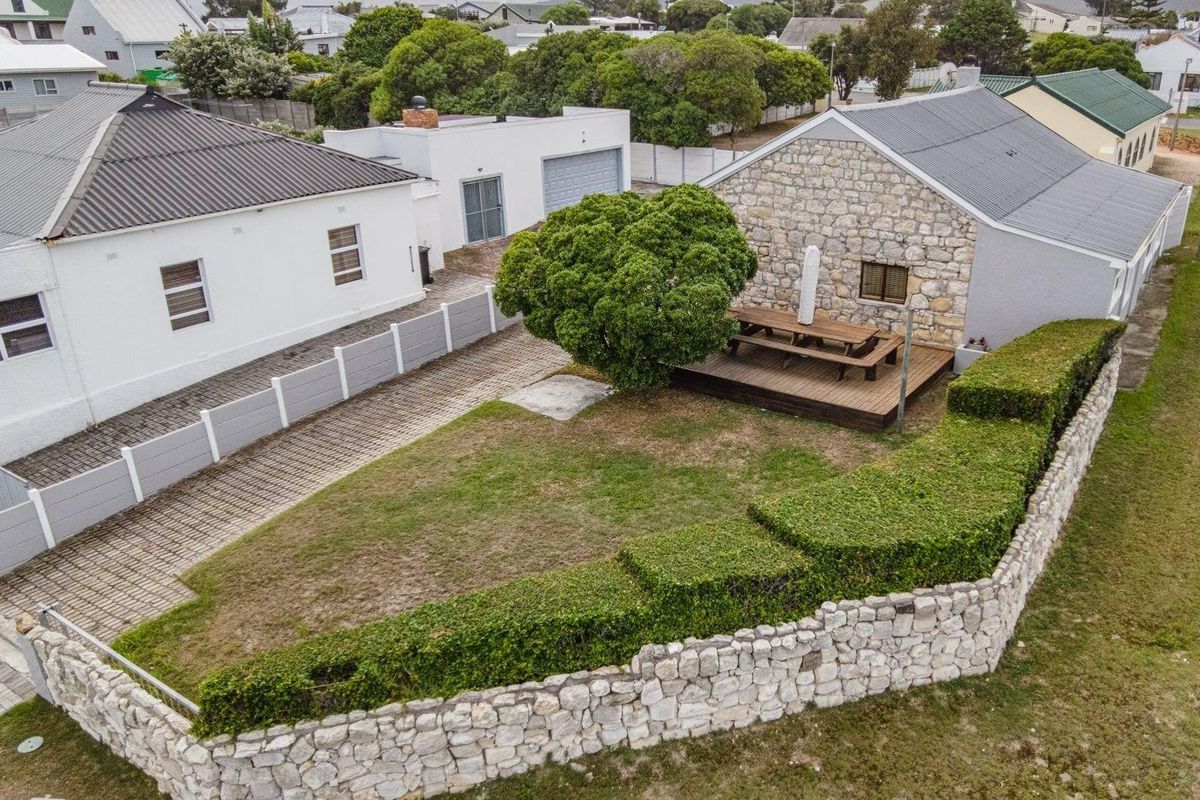 Aerial view of the property featuring a stone-clad exterior, a wooden deck, a paved driveway, and a well-maintained garden with a stone boundary wall.