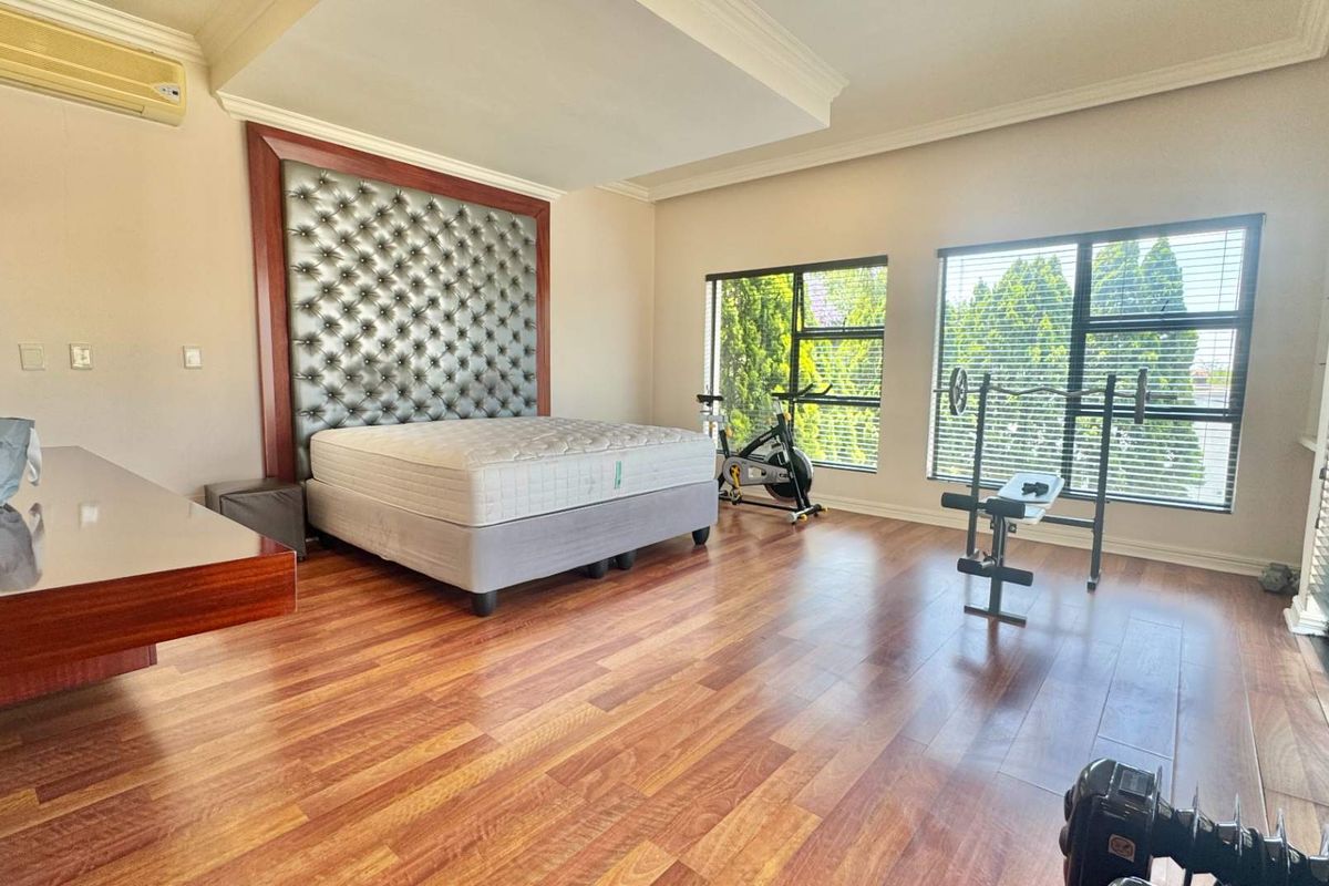 Spacious bedroom featuring warm wood-look flooring, large windows with fitted blinds, a built-in headboard feature, and a wall-mounted air conditioning unit.