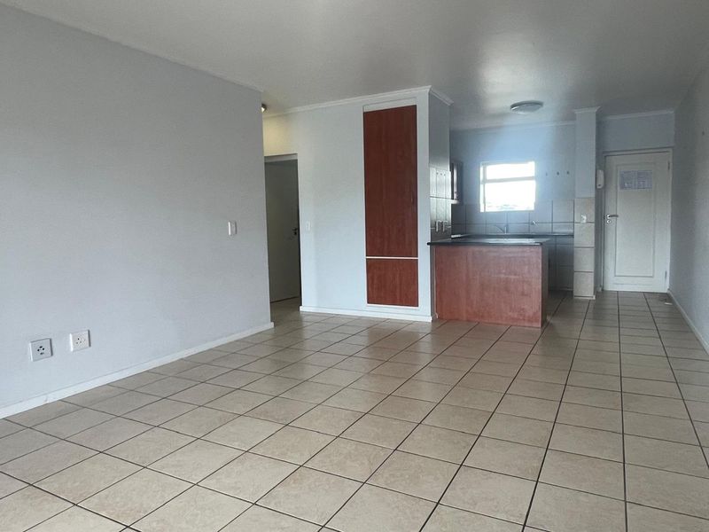 An open-plan living and kitchen area featuring neutral tiled flooring, built-in cabinetry, and a breakfast bar, offering a clean and functional layout.