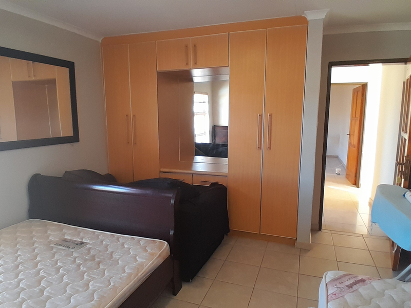 A bedroom featuring built-in wooden cupboards with a central vanity mirror and tiled flooring, leading to an adjacent hallway.