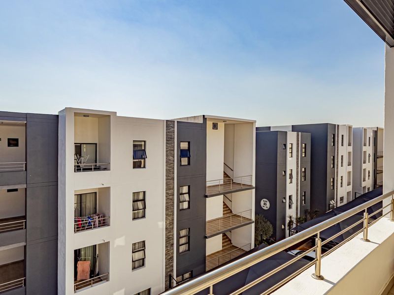 A view from a modern apartment balcony overlooking the surrounding residential complex buildings with clean architectural lines and stainless steel railings.