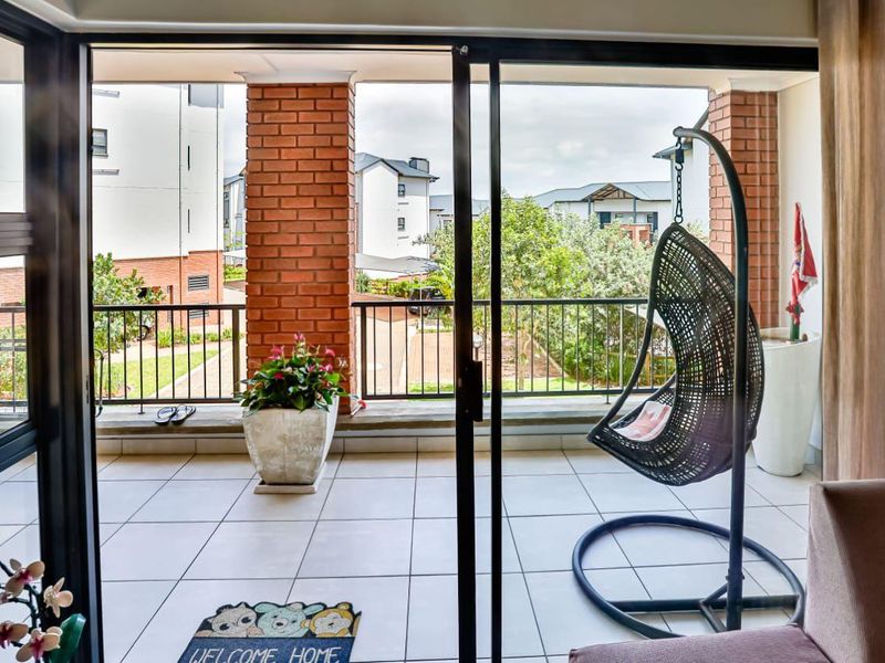 A covered balcony featuring tiled flooring, brick support pillars, and metal railings, accessible through large sliding glass doors.