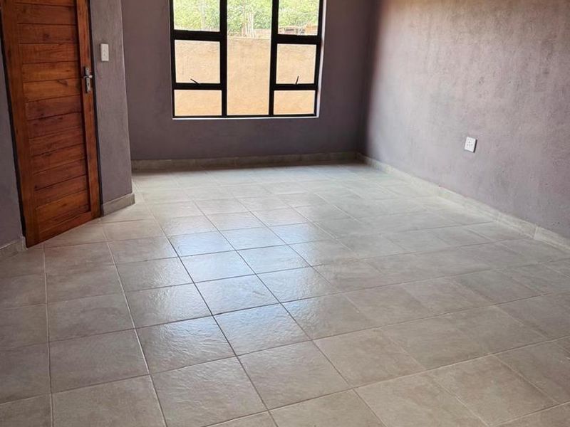 An empty living room featuring tiled flooring, a timber door, and aluminium window frames, providing a blank canvas for interior design.