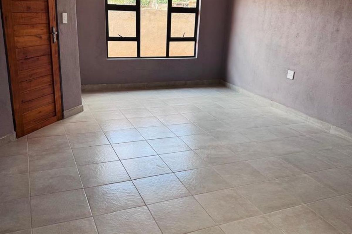 An empty living room featuring tiled flooring, a timber door, and aluminium window frames, providing a blank canvas for interior design.
