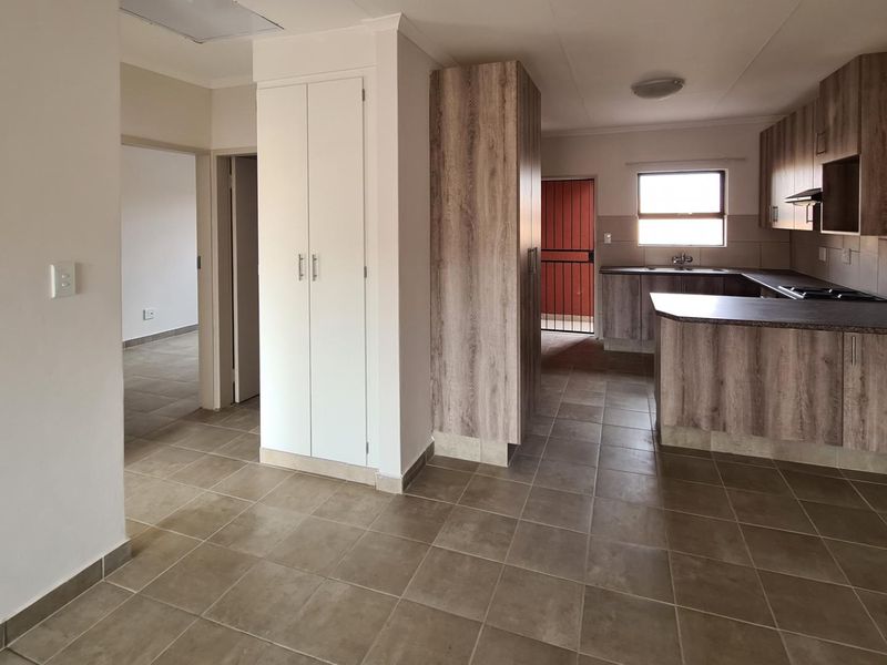 Open-plan living area featuring tiled flooring, built-in kitchen cabinetry with hob and extractor, and access to a secure exterior door.