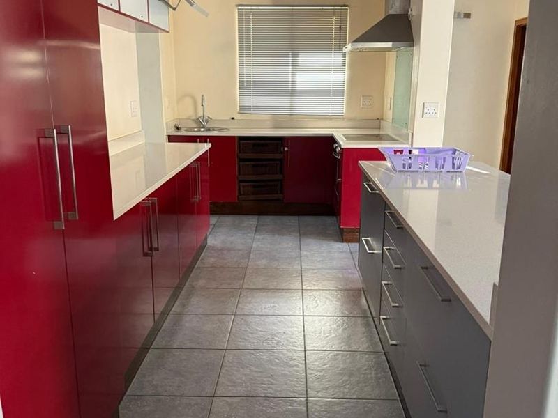 A functional kitchen featuring red and grey cabinetry, stone countertops, stainless steel extractor fan, and tiled flooring.