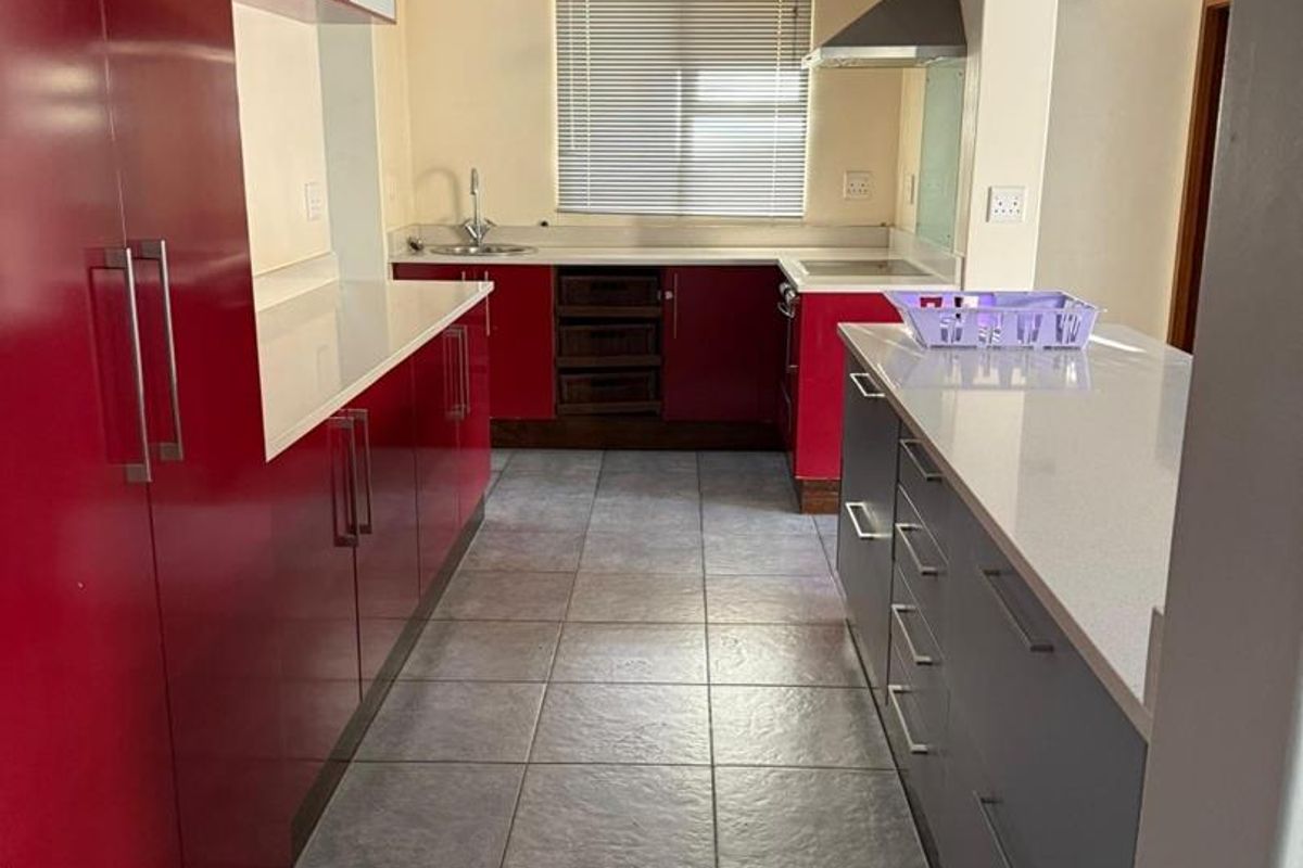 A functional kitchen featuring red and grey cabinetry, stone countertops, stainless steel extractor fan, and tiled flooring.