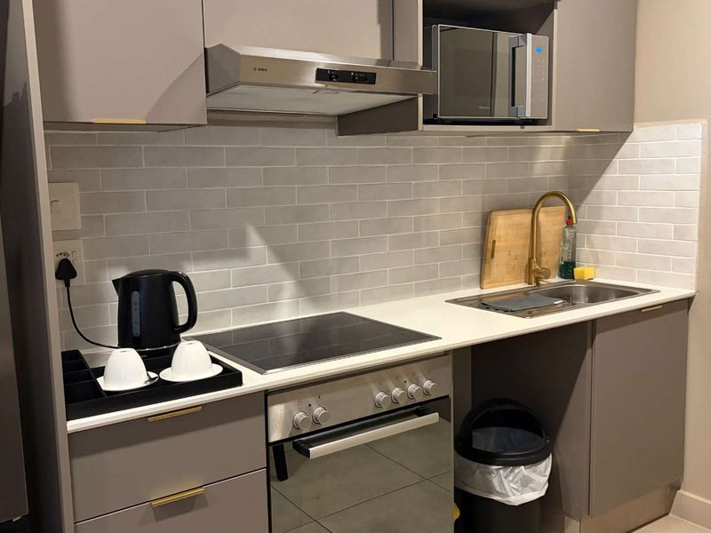 Modern kitchen featuring grey cabinetry, subway tile backsplash, stone countertops, and integrated appliances including an oven, hob, and microwave.