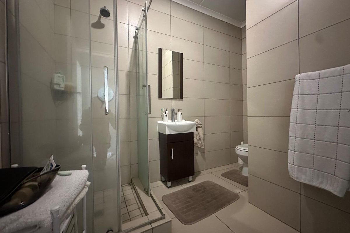 A compact bathroom featuring a glass-enclosed shower, a wall-mounted vanity with a basin, and a toilet, finished with neutral floor-to-ceiling wall tiles.
