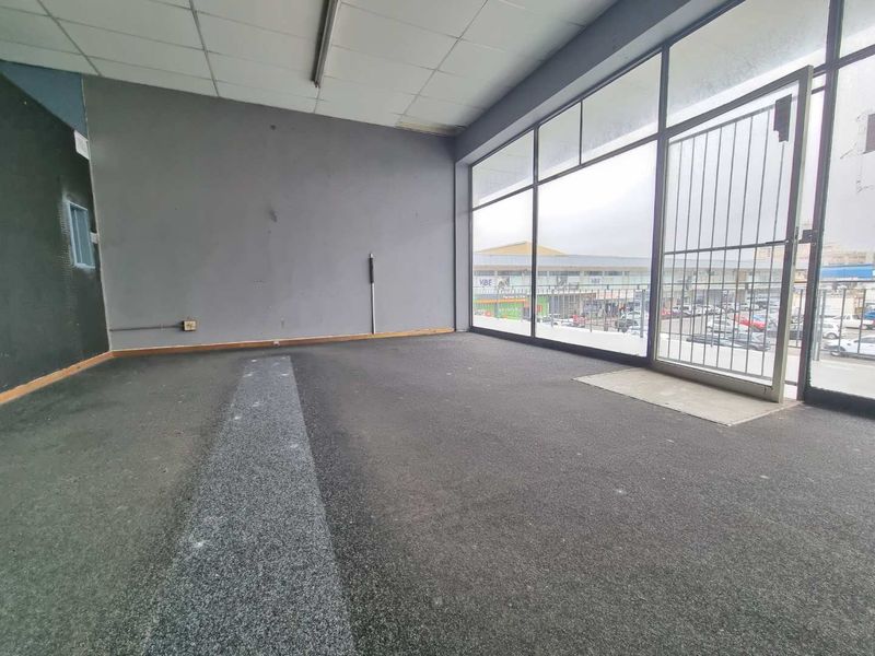 Empty commercial office space featuring large glass storefront windows, security gate, suspended ceiling, and carpeted flooring, suitable for retail or professional use.