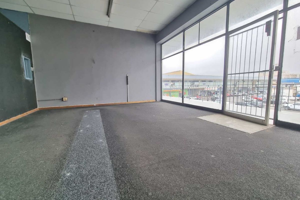 Empty commercial office space featuring large glass storefront windows, security gate, suspended ceiling, and carpeted flooring, suitable for retail or professional use.