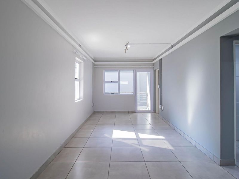 A bright, empty living area featuring neutral tiled flooring, cove ceiling detailing, and access to an outdoor space through an aluminium door.