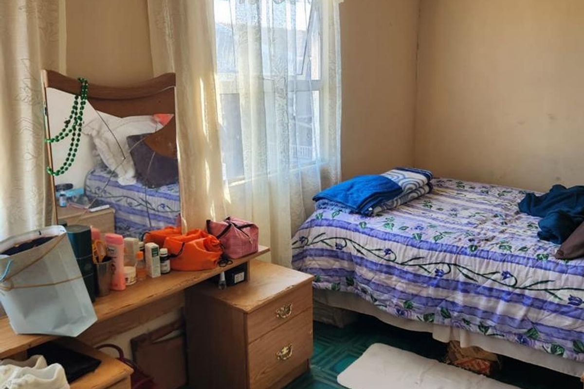 A bedroom featuring a window with curtains and dated floor finishes, providing a functional sleeping space.