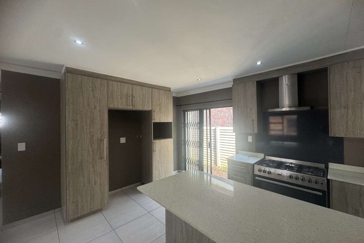 Modern kitchen featuring wood-grain cabinetry, stone countertops, a gas stove with extractor fan, and direct access to the outdoor area through sliding doors.