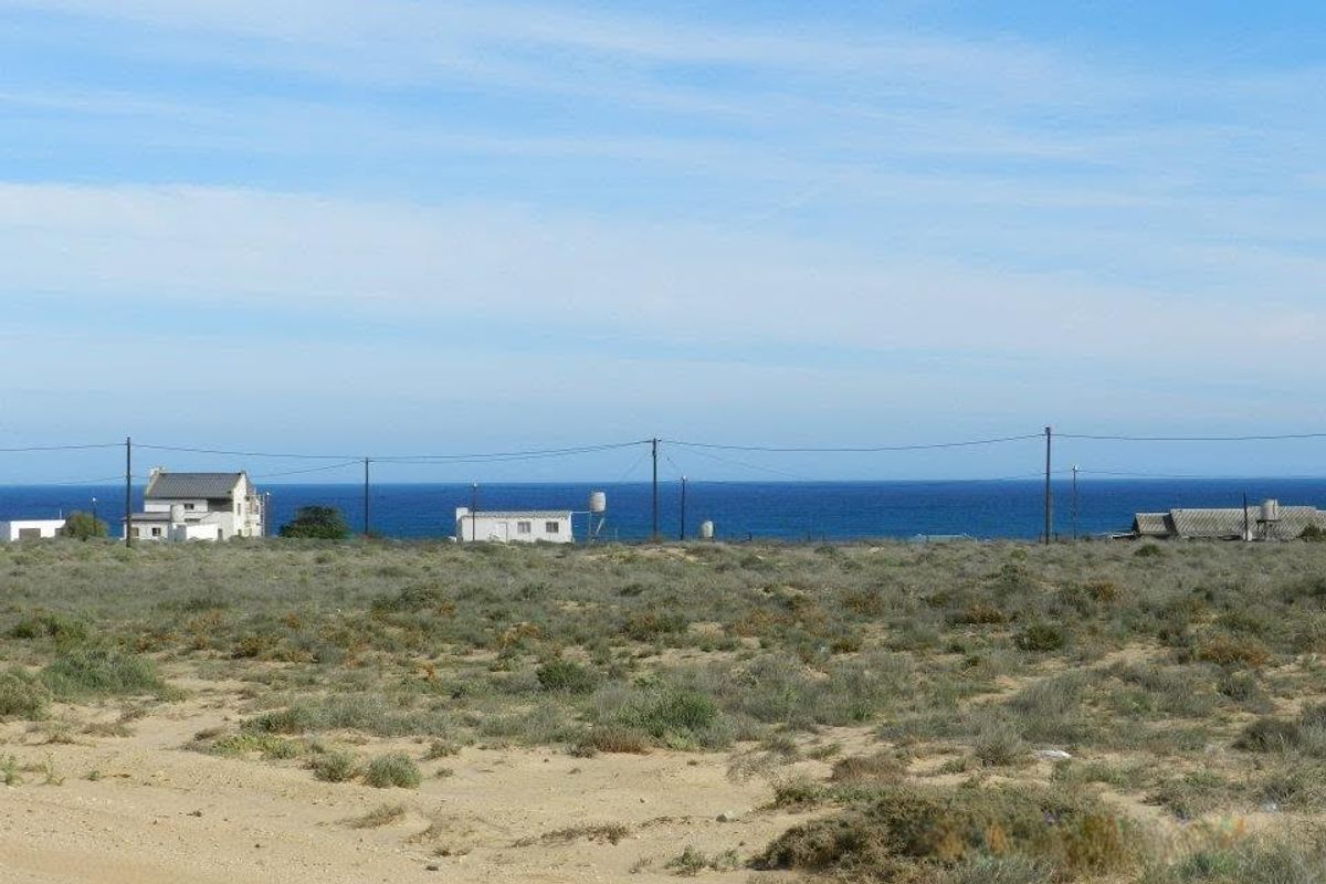 A wide-angle view of a vacant residential plot featuring natural coastal vegetation with distant ocean views and neighboring properties.