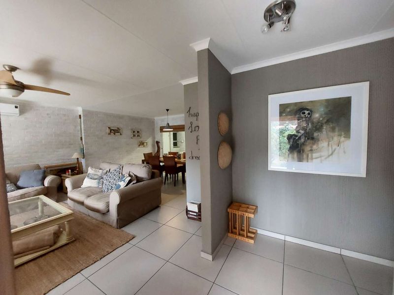 Open-plan living and dining area featuring tiled floors, a brick feature wall, ceiling fan, and air conditioning unit.