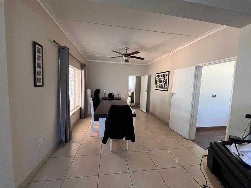 A functional dining room featuring neutral tiled flooring, a ceiling fan, and direct access to adjacent rooms through standard internal doors.