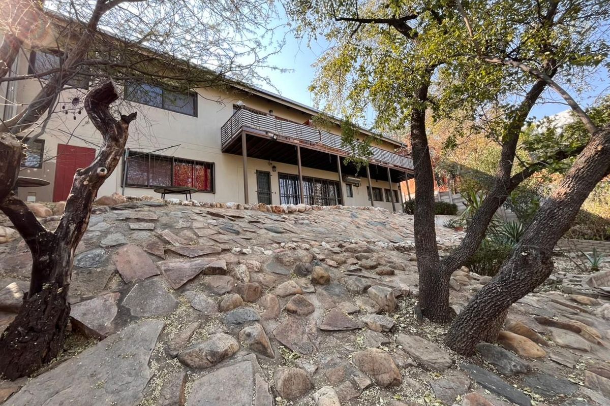 Rear view of the property featuring a raised balcony with metal balustrade, stone retaining wall, and established garden landscaping.