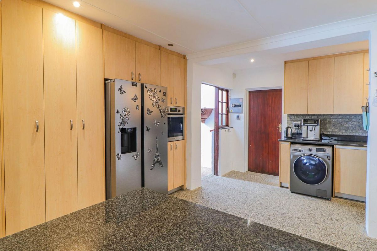 A functional kitchen featuring light wood cabinetry, granite countertops, and integrated appliance spaces, leading to a separate utility or laundry area.