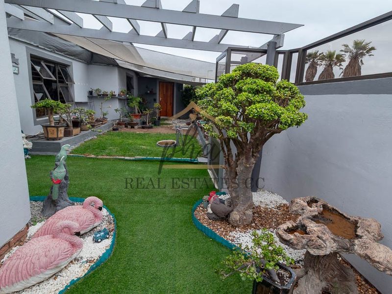 A private outdoor patio area featuring a pergola structure, artificial lawn, and landscaped garden beds.