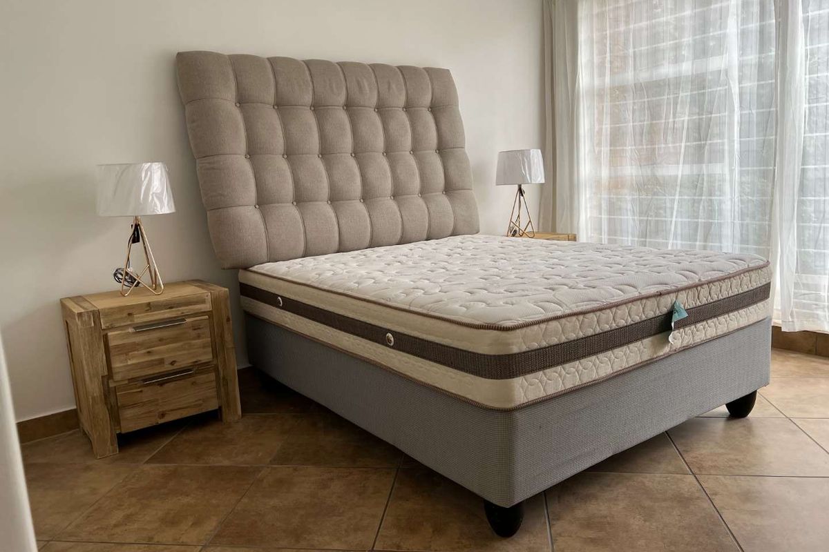 A well-lit bedroom featuring tiled flooring and a large window with sheer curtains, providing a bright and neutral space.