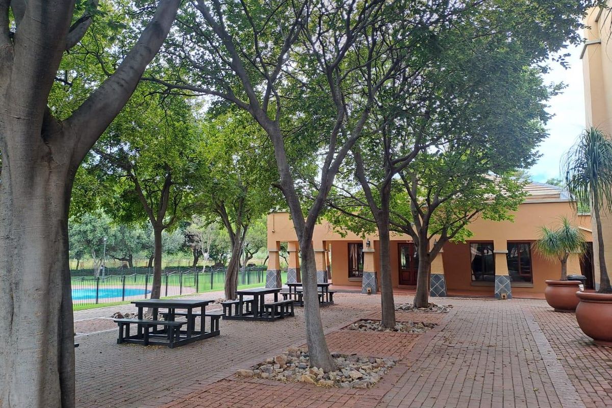 A well-maintained communal courtyard area featuring paved walkways, mature trees, a covered patio space, and access to a swimming pool.