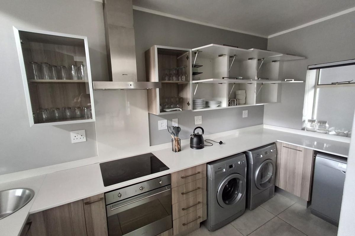 Modern kitchen featuring sleek laminate cabinetry, quartz countertops, built-in oven, electric hob, stainless steel extractor fan, and integrated laundry appliance space.