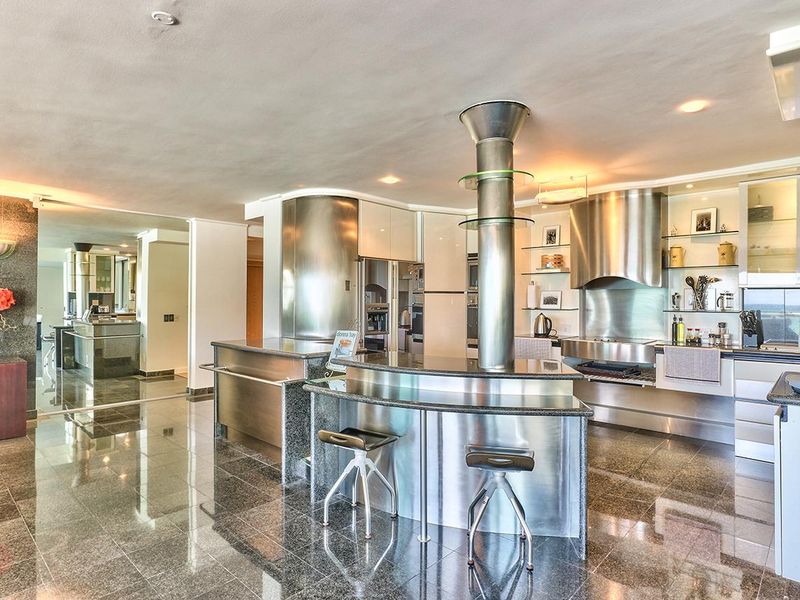 Modern kitchen featuring high-end stainless steel cabinetry, granite countertops, a central breakfast bar, and premium built-in appliances with polished stone flooring.