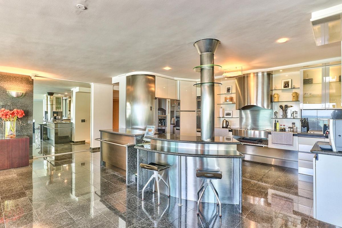 Modern kitchen featuring high-end stainless steel cabinetry, granite countertops, a central breakfast bar, and premium built-in appliances with polished stone flooring.