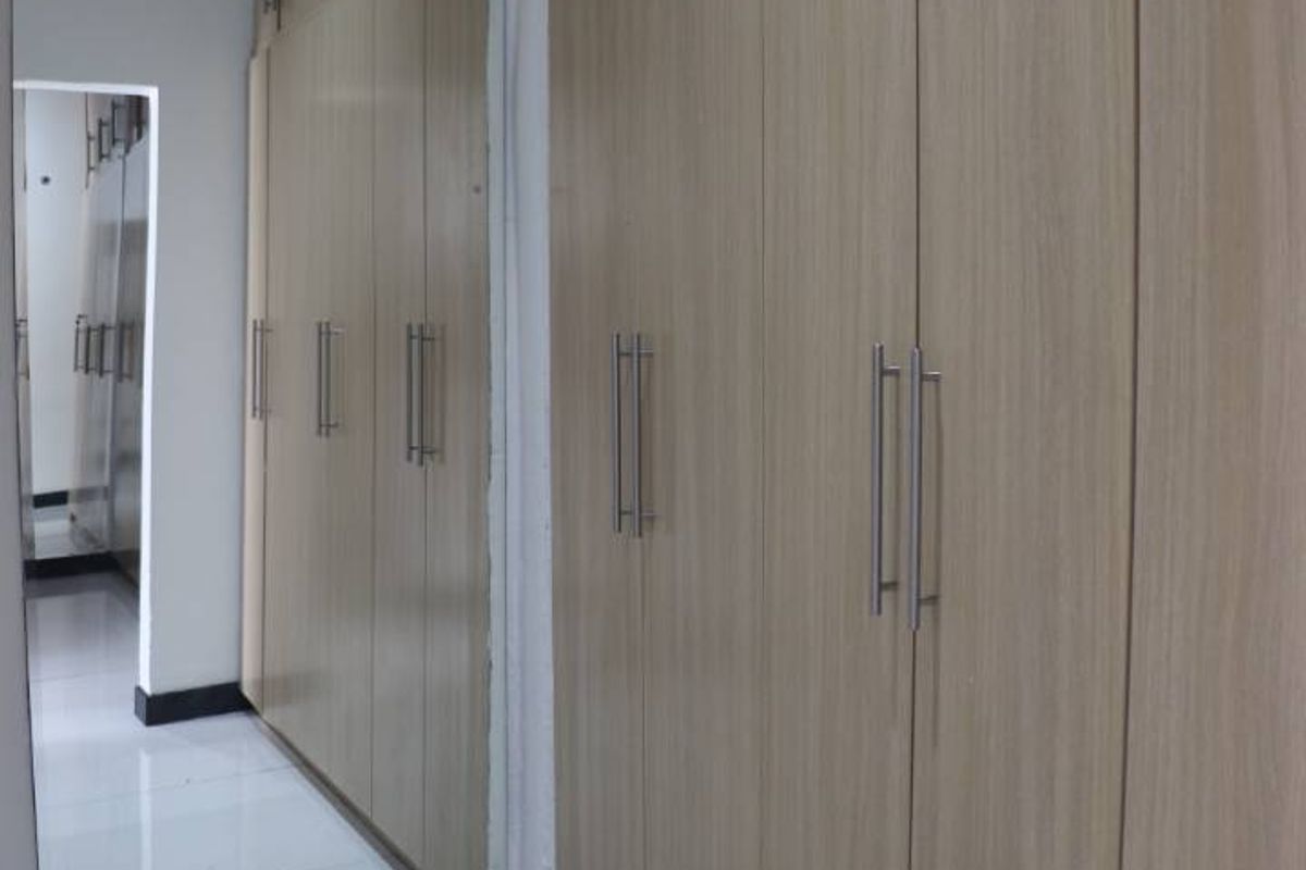 A bedroom featuring extensive built-in wooden cupboards with integrated mirrored doors and clean white tiled flooring.