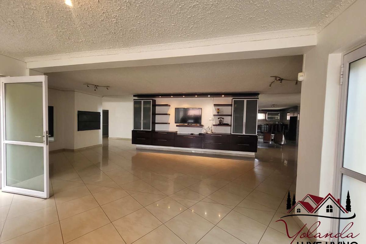 Spacious open-plan living area featuring large format floor tiles, built-in dark wood cabinetry, and integrated display shelving.