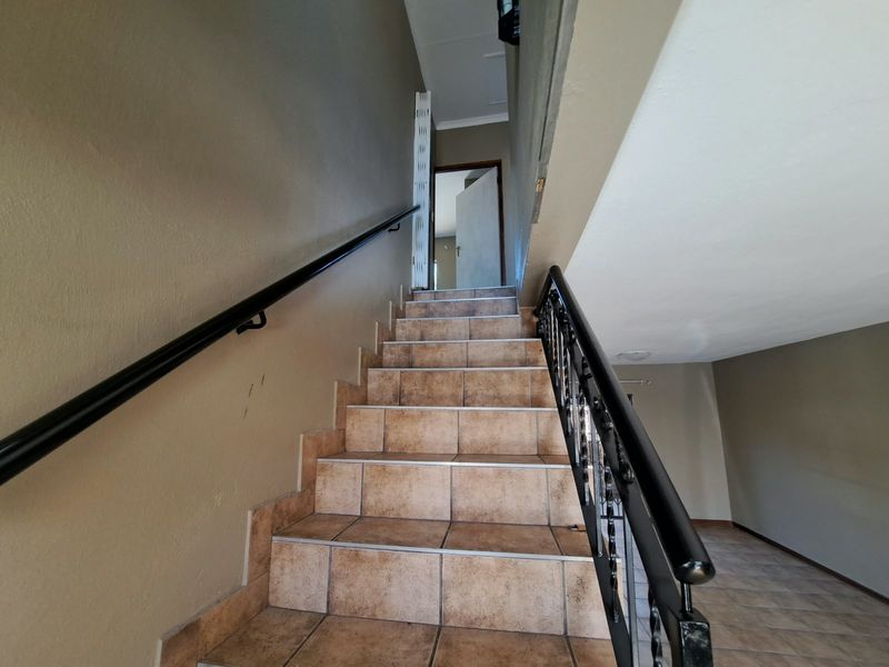 A staircase featuring tiled steps, a black wrought iron balustrade, and a wall-mounted handrail leading to an upper level.