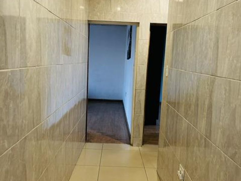 A clean, tiled hallway featuring neutral wall tiles, floor tiles, and decorative ceiling molding, providing a bright transition between interior rooms.