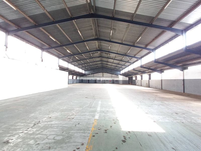 Spacious industrial warehouse featuring high ceilings, exposed steel trusses, ample natural light through clerestory windows, and durable concrete flooring.