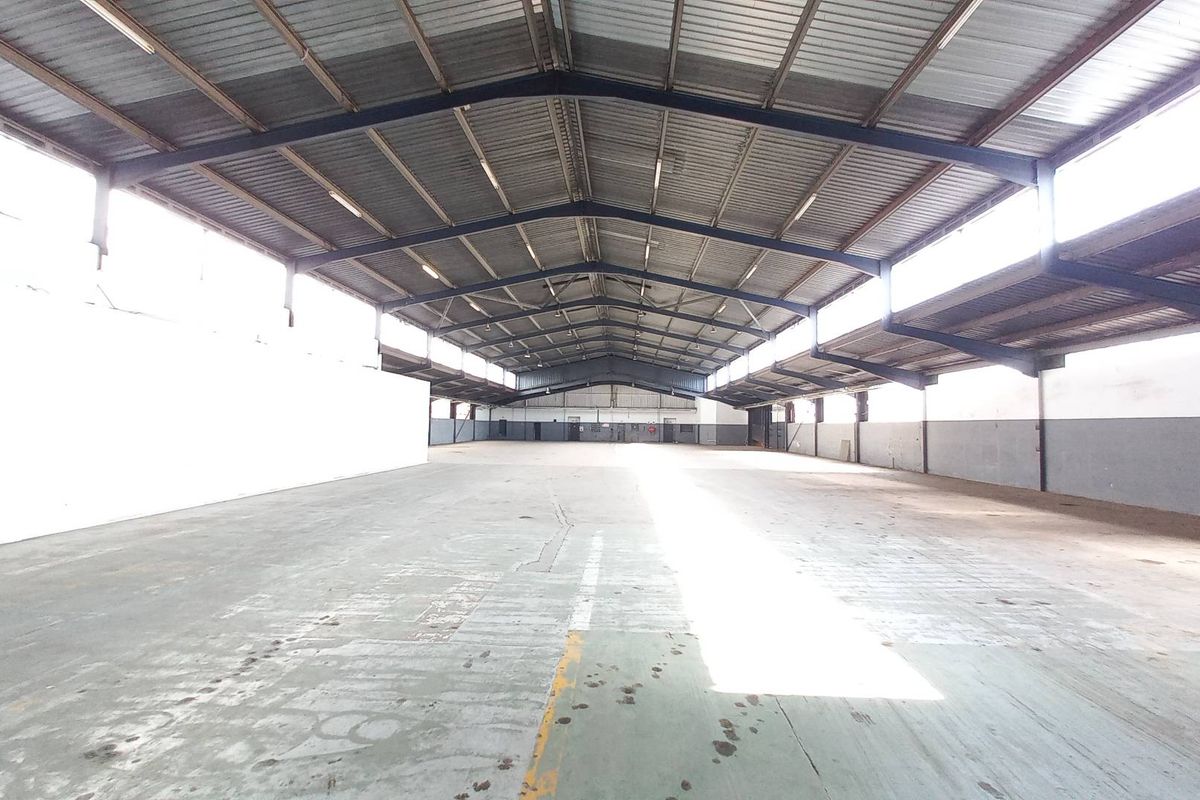 Spacious industrial warehouse featuring high ceilings, exposed steel trusses, ample natural light through clerestory windows, and durable concrete flooring.