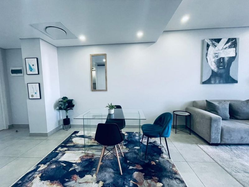 A modern open-plan living and dining area featuring neutral porcelain floor tiles, recessed ceiling lighting, and integrated air conditioning.