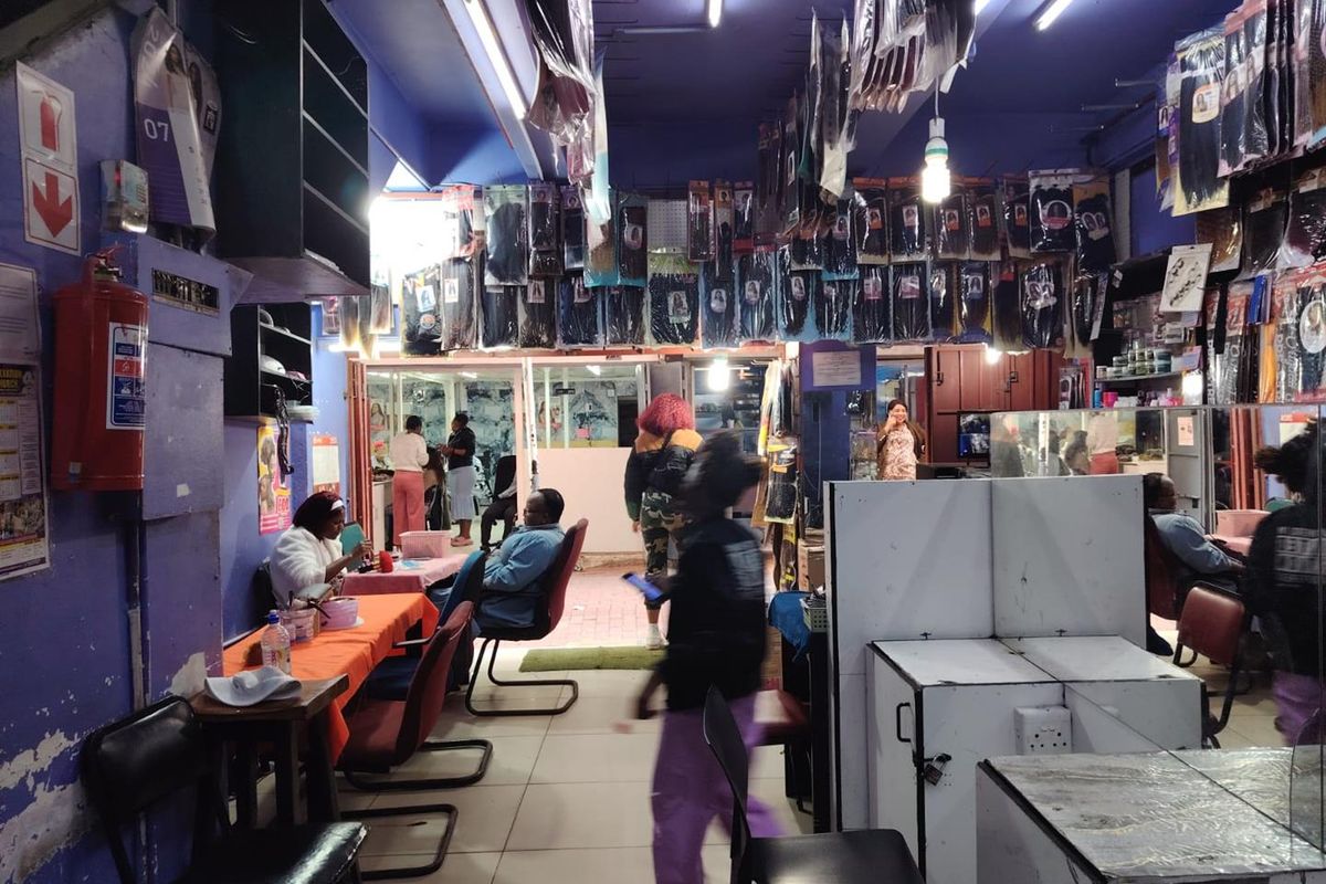 Interior view of a retail hair salon space featuring tiled floors, fluorescent lighting, and wall-mounted shelving units.