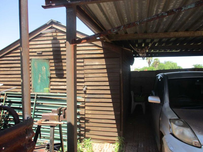 A weathered timber utility shed with a corrugated metal roof and steel support structure, showing signs of age and surface corrosion.