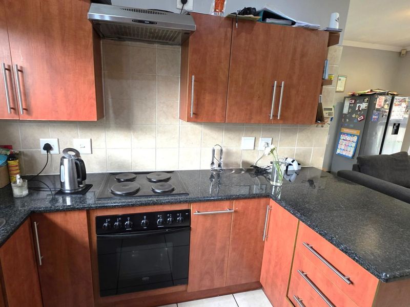A functional kitchen featuring granite countertops, built-in oven, electric hob, extractor fan, and ample laminate cabinetry with a tiled backsplash.