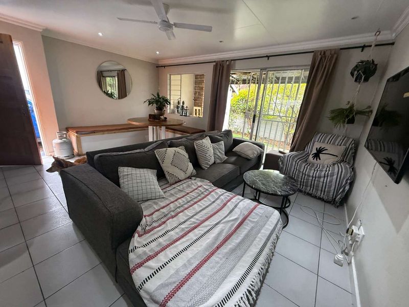 A comfortable living room featuring tiled flooring, a ceiling fan, and sliding glass doors that provide access to the outdoor area.
