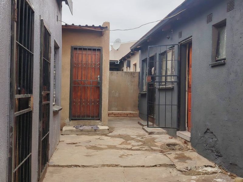 A narrow rear exterior courtyard area featuring concrete paving, security gates, and exterior wall access points.