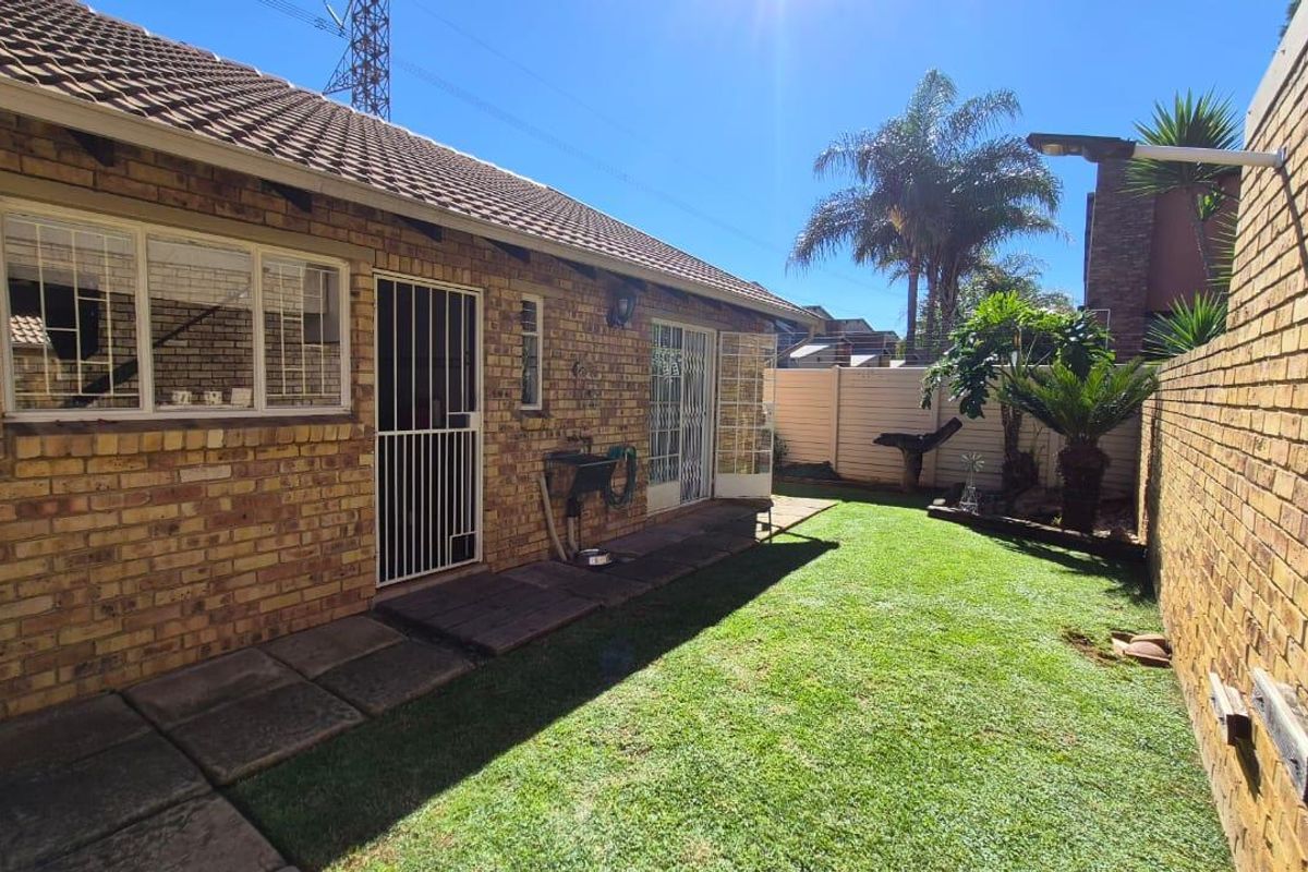 A private rear garden featuring a brick townhouse exterior, paved walkway, and established lawn area.