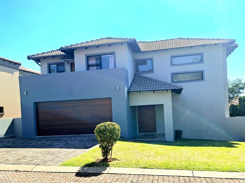 A modern double-story residential home featuring a paved driveway, double garage, and a well-maintained front garden.