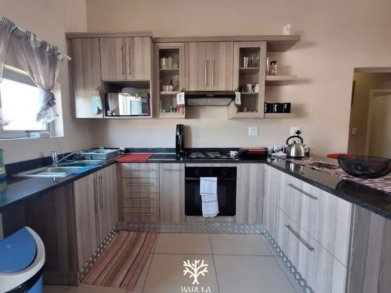 A functional kitchen featuring wood-look cabinetry, granite countertops, a built-in oven with gas hob, and tiled flooring.