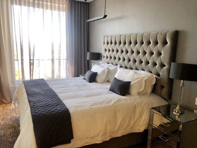 A well-appointed bedroom featuring a large window with floor-to-ceiling curtains, modern pendant lighting, and a neutral color palette.
