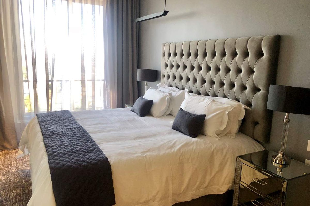 A well-appointed bedroom featuring a large window with floor-to-ceiling curtains, modern pendant lighting, and a neutral color palette.