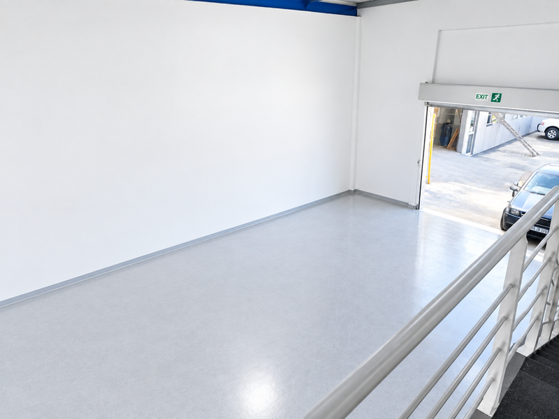 A clean, empty utility or warehouse space featuring durable epoxy flooring, a metal safety railing, and a large roller shutter door for easy access.
