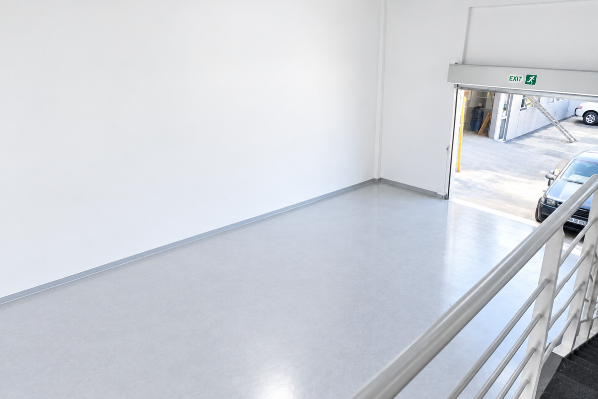 A clean, empty utility or warehouse space featuring durable epoxy flooring, a metal safety railing, and a large roller shutter door for easy access.