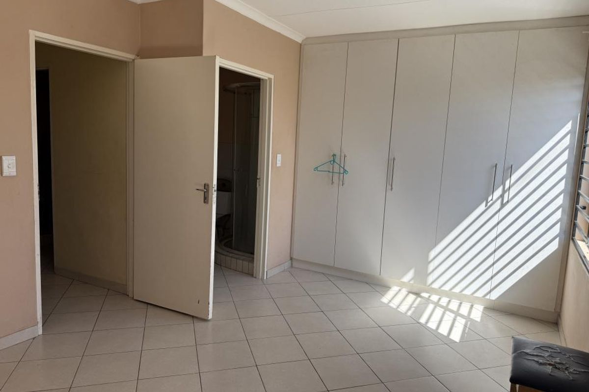 A bedroom featuring built-in cupboards, tiled flooring, and an en-suite bathroom entrance, offering a functional and neutral living space.