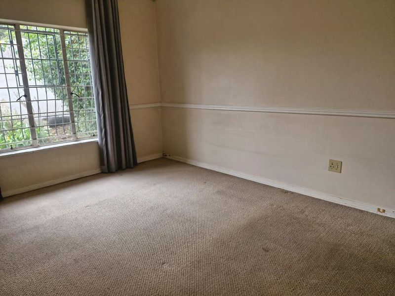An empty bedroom featuring neutral walls with chair rail molding, carpeted flooring, and a window fitted with security bars.